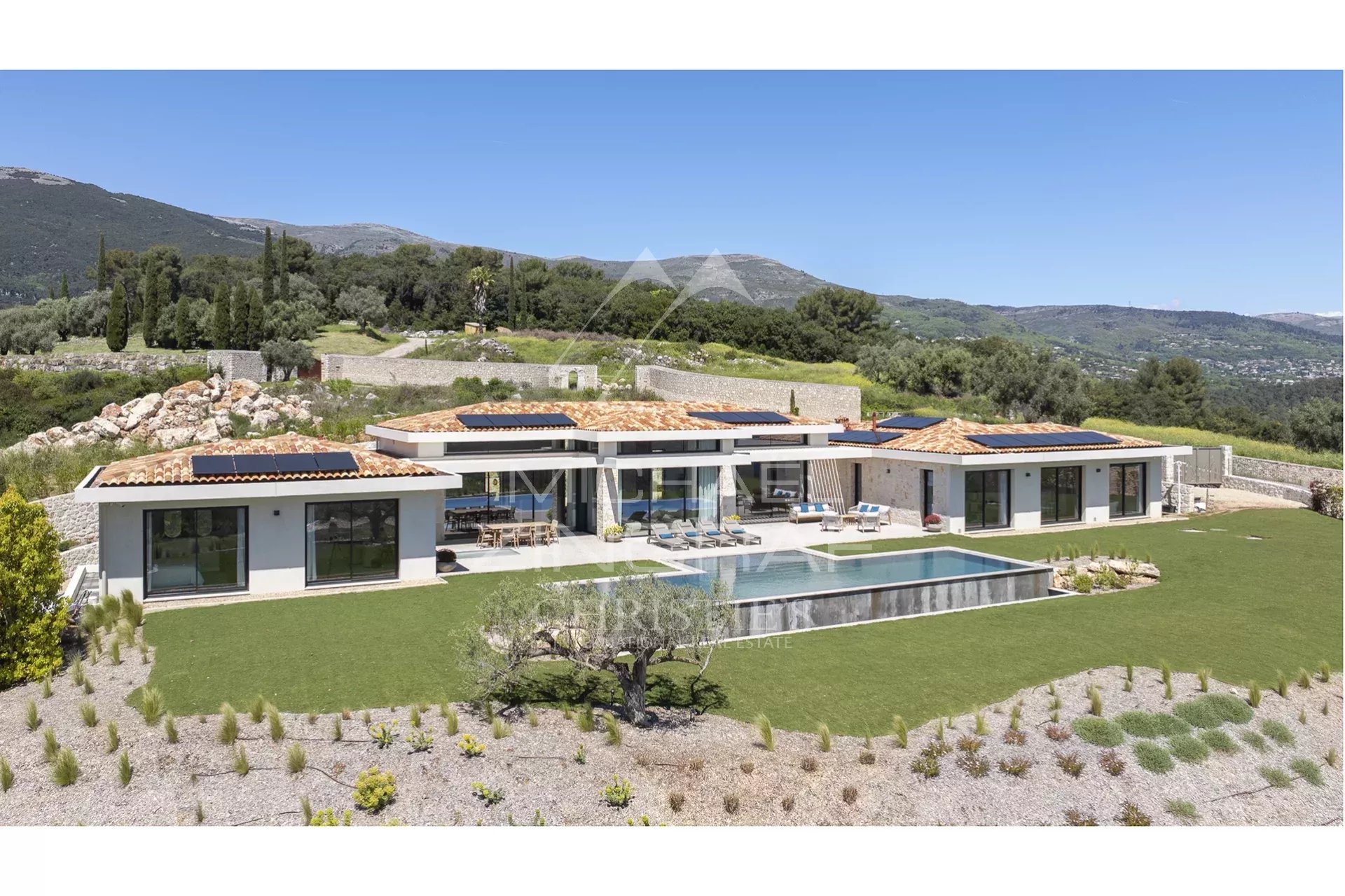 Modern single-story villa with orange-tiled roof, solar panels, and a rectangular pool in a landscaped countryside setting.