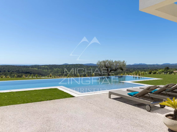 Infinity pool with white coping and lounge chairs, overlooking rolling green hills under a clear blue sky at a luxury outdoor space.