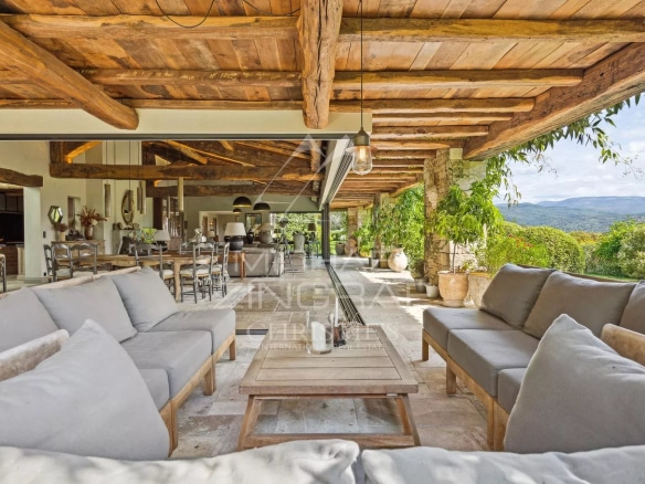 Terrasse d'une villa en Provence avec vue sur la vallée et des villages perchés, mobilier en bois et coussins gris.