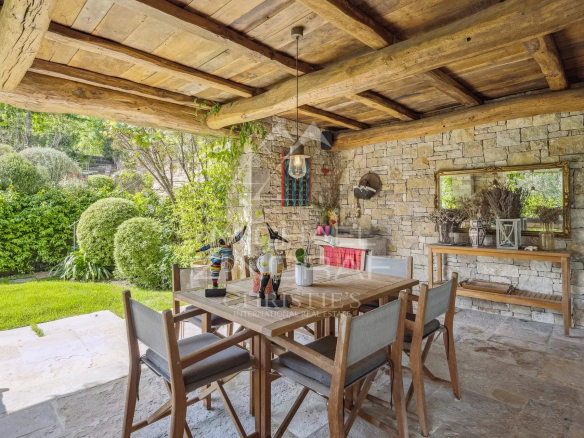 Terrasse d'une villa en Provence avec table en bois et chaises, entourée de verdure.