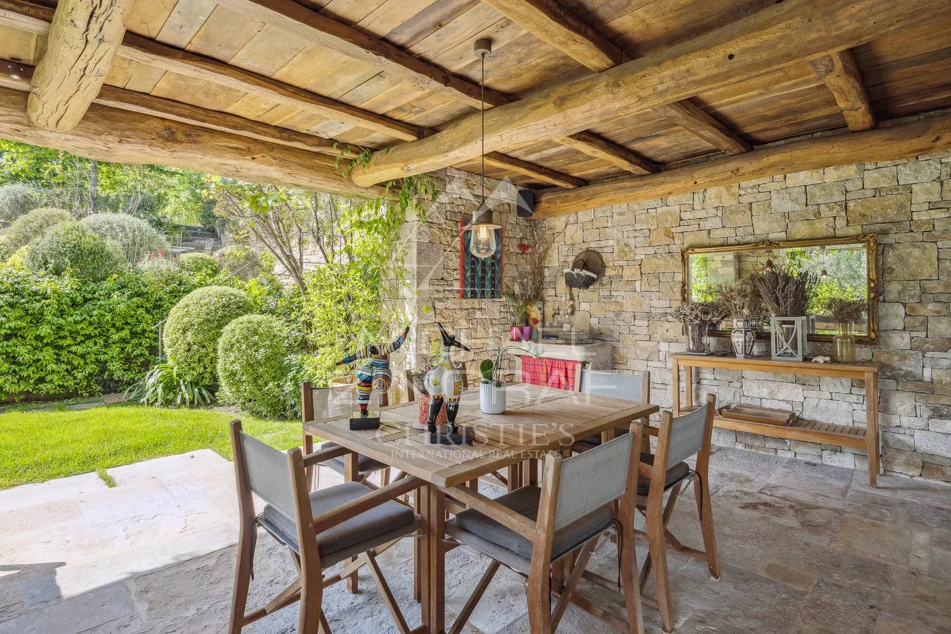 Terrasse d'une villa en Provence avec table en bois et chaises, entourée de verdure.