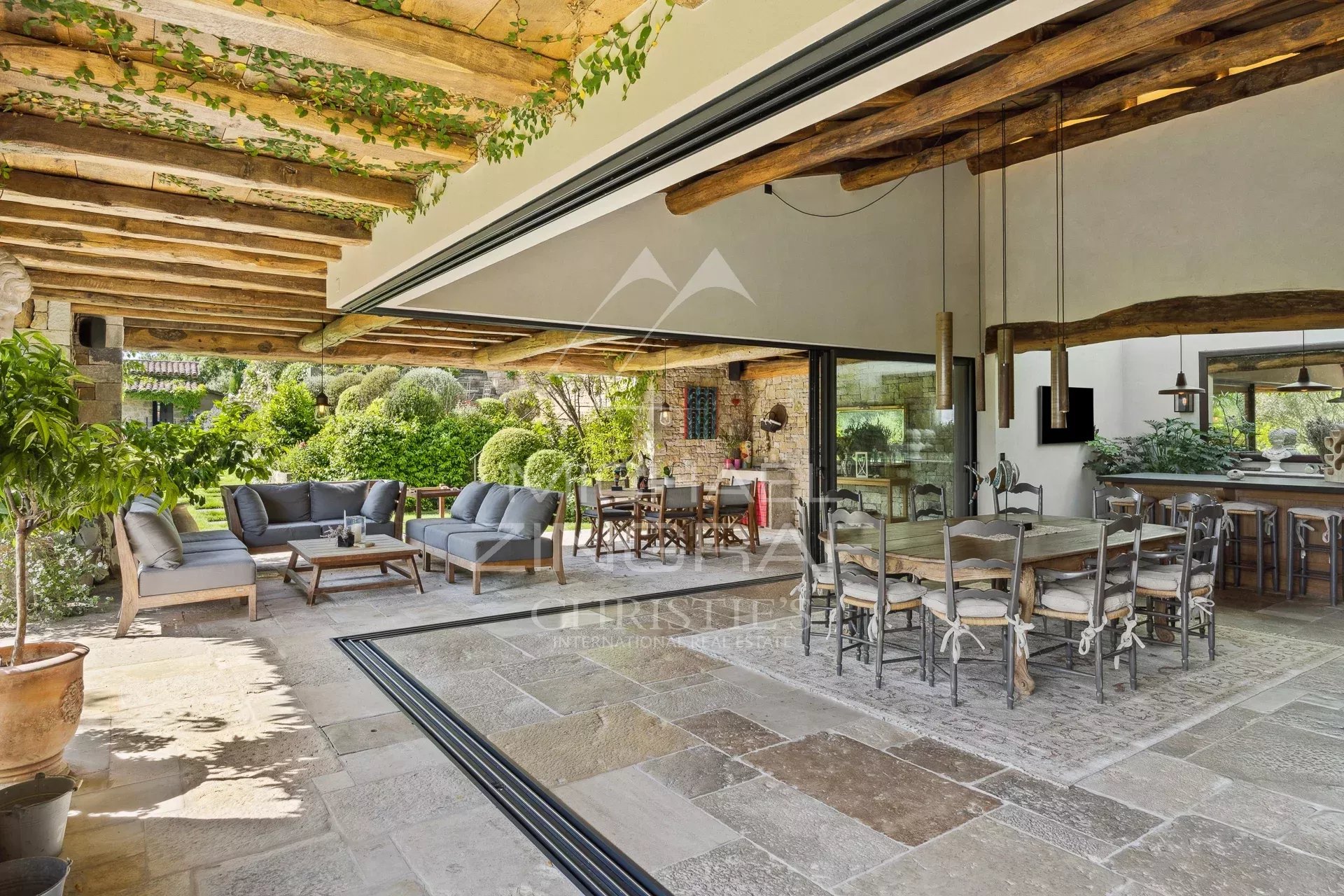 Terrasse d'une villa en Provence avec mobilier extérieur et vue sur un jardin verdoyant.