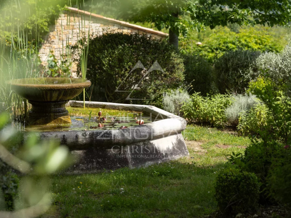 Fontaine dans un jardin verdoyant avec des plantes aromatiques et des fleurs.