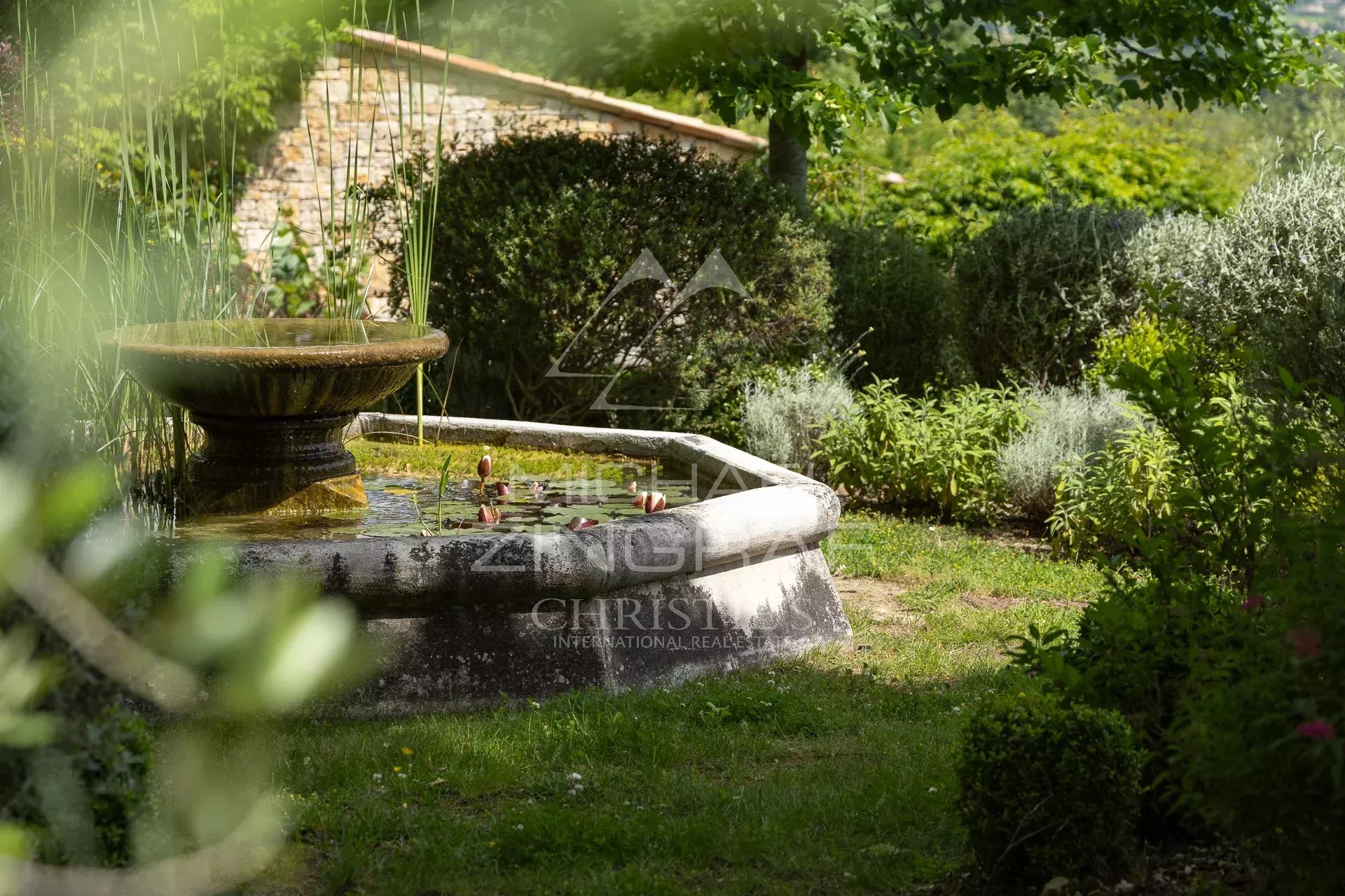 Fontaine dans un jardin verdoyant avec des plantes aromatiques et des fleurs.