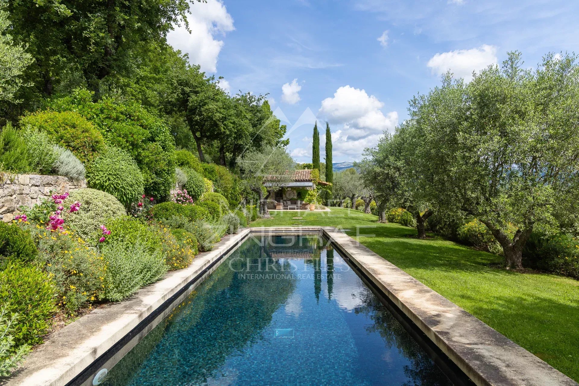 Vue d'une villa de plain-pied avec piscine et jardin en Provence, entourée d'arbres et de fleurs.