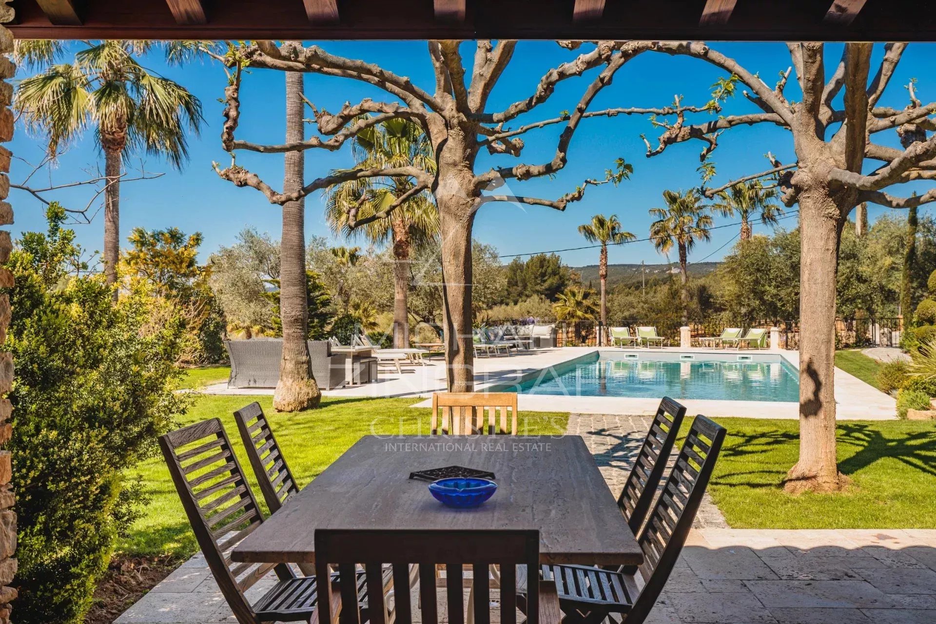 Domaine provençal avec piscine Terrasse avec table en bois et piscine entourée de palmiers dans un domaine provençal.