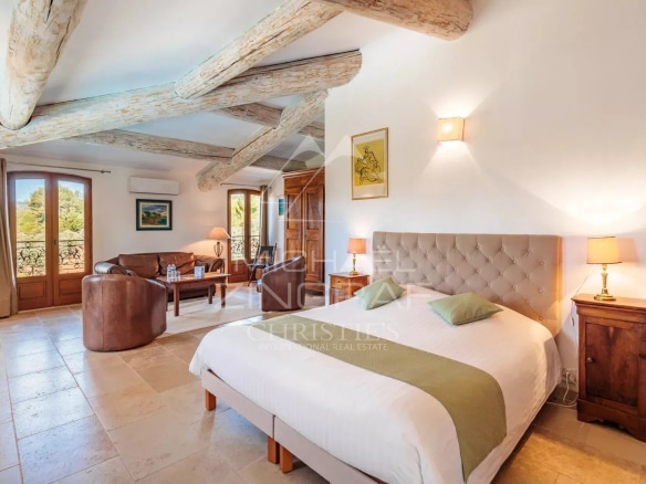 Chambre spacieuse avec lit double, canapés et poutres apparentes dans un domaine provençal.