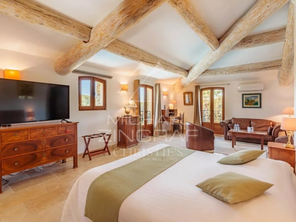 Chambre spacieuse d'un domaine provençal avec lit, télévision et mobilier en bois.