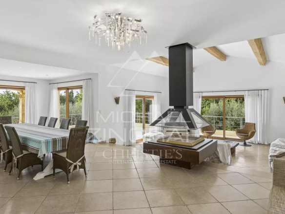 Intérieur d'une villa contemporaine avec salle à manger et cheminée, fenêtres donnant sur un jardin.