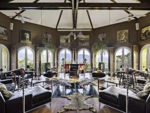 Intérieur d'une propriété de luxe avec salon spacieux et grandes fenêtres offrant une vue sur la nature.