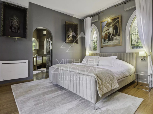 Chambre élégante avec lit double et décoration artistique, murs gris, fenêtres en arc.