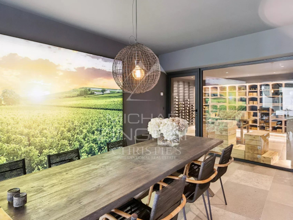 Salle à manger moderne avec vue sur un paysage viticole, éclairage suspendu et cave à vin.