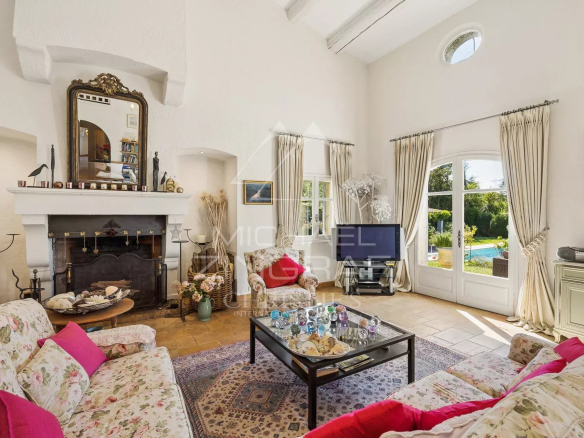 Intérieur d'une villa provençale avec salon lumineux et cheminée, décoré de fleurs et d'œuvres d'art.