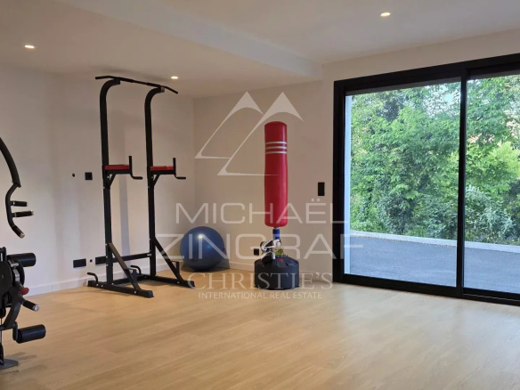 Salle de sport moderne avec équipements de fitness et grande baie vitrée donnant sur l'extérieur.