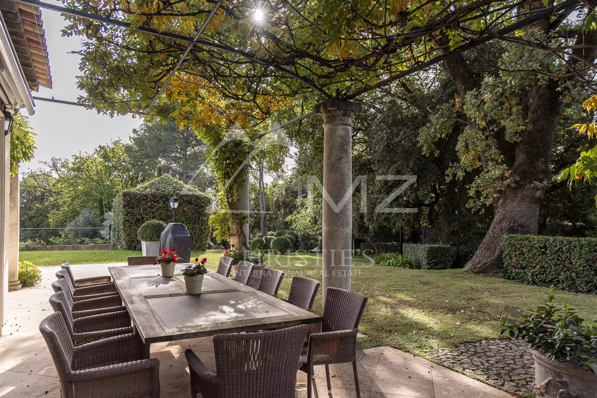 Terrasse de la Bastide Aixoise Terrasse d'une bastide aixoise avec table et chaises, entourée de verdure dans un parc paysager.
