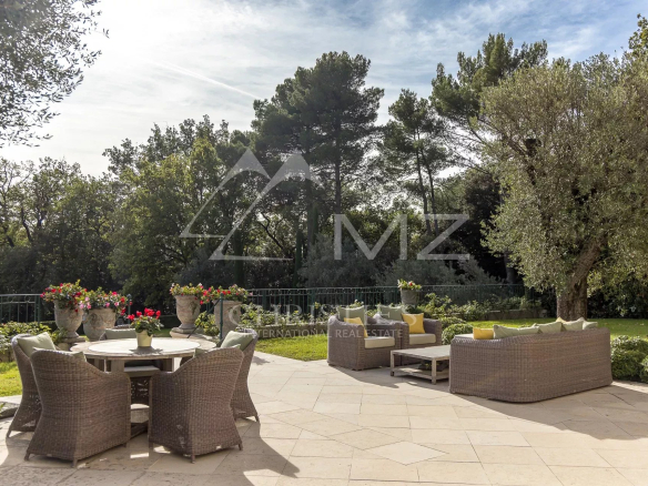 Terrasse d'une bastide aixoise avec mobilier en osier et vue sur un parc arboré.