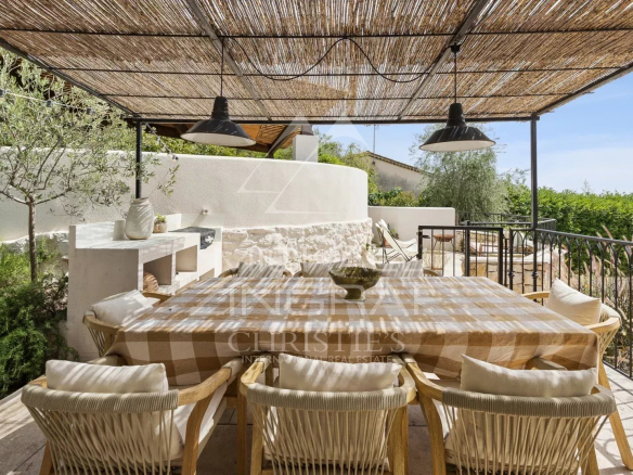 Sunny terrace with dining table and chairs, surrounded by greenery, in Le Rouret.