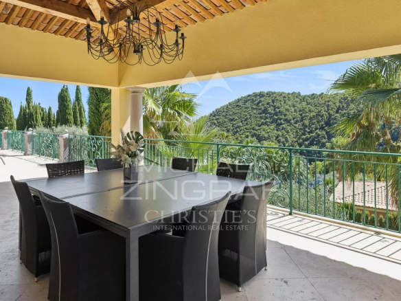 Terrasse d'une villa à Grasse avec vue sur la nature, mobilier de jardin et piscine visible au loin.