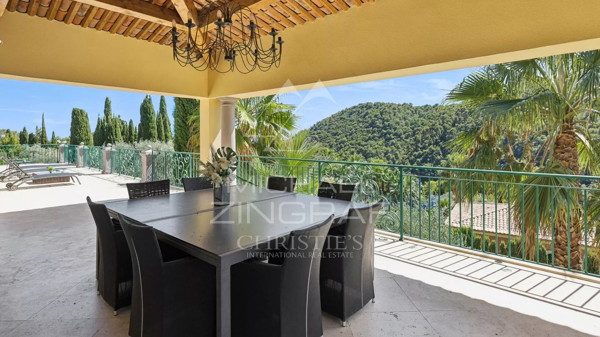 Terrasse d'une villa à Grasse avec vue sur la nature, mobilier de jardin et piscine visible au loin.