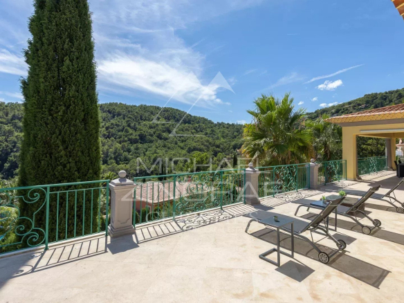 Terrasse d'une villa à Grasse avec chaises longues et vue sur les collines verdoyantes.