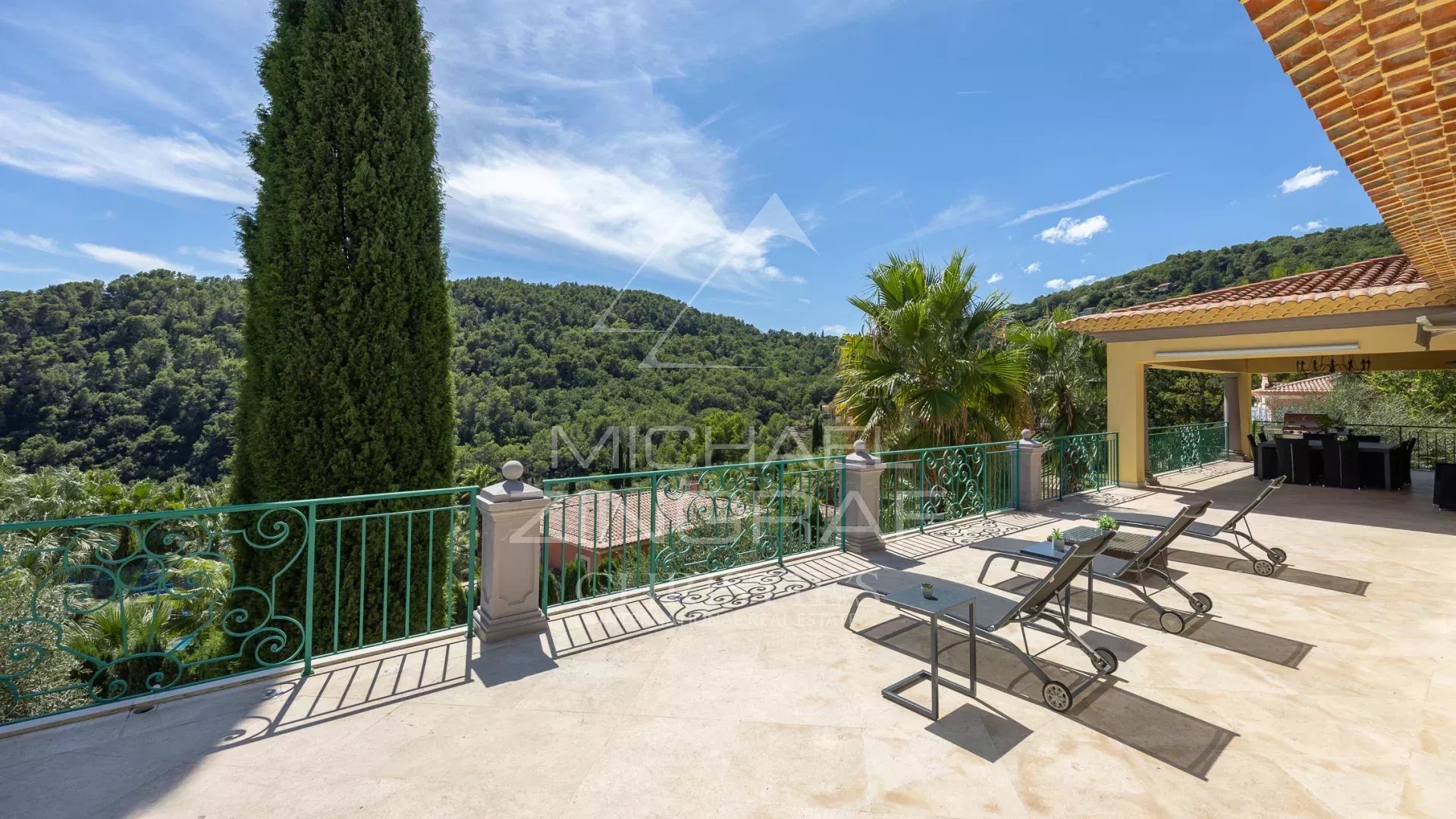 Terrasse d'une villa à Grasse avec chaises longues et vue sur les collines verdoyantes.