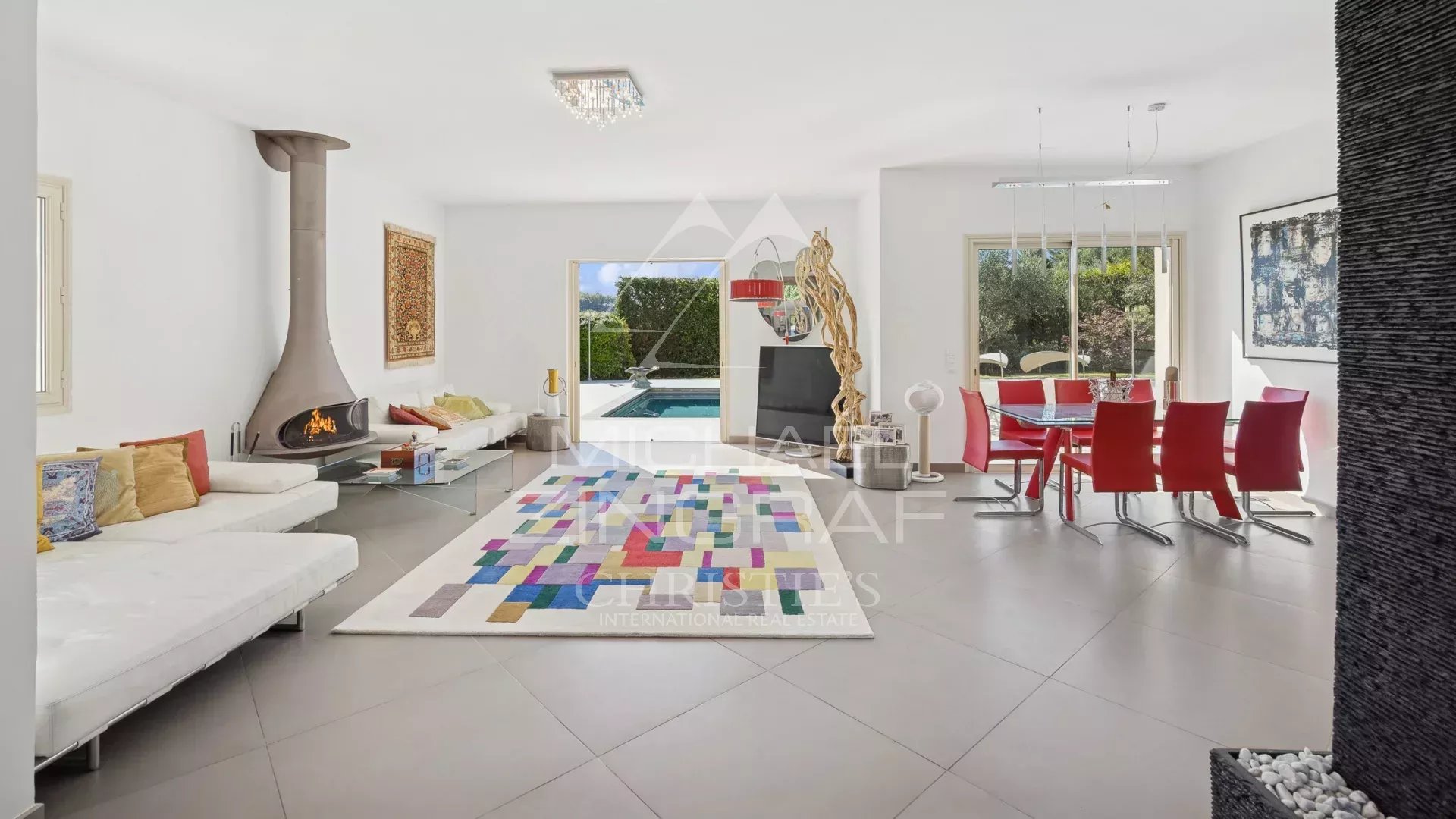 Intérieur d'une villa moderne avec salon et salle à manger, piscine visible à l'extérieur.