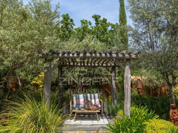 Wooden pergola with plants and seating in a lush garden in Draguignan.