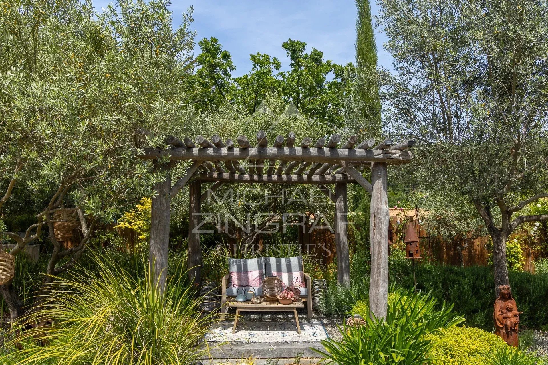 Wooden pergola with plants and seating in a lush garden in Draguignan.