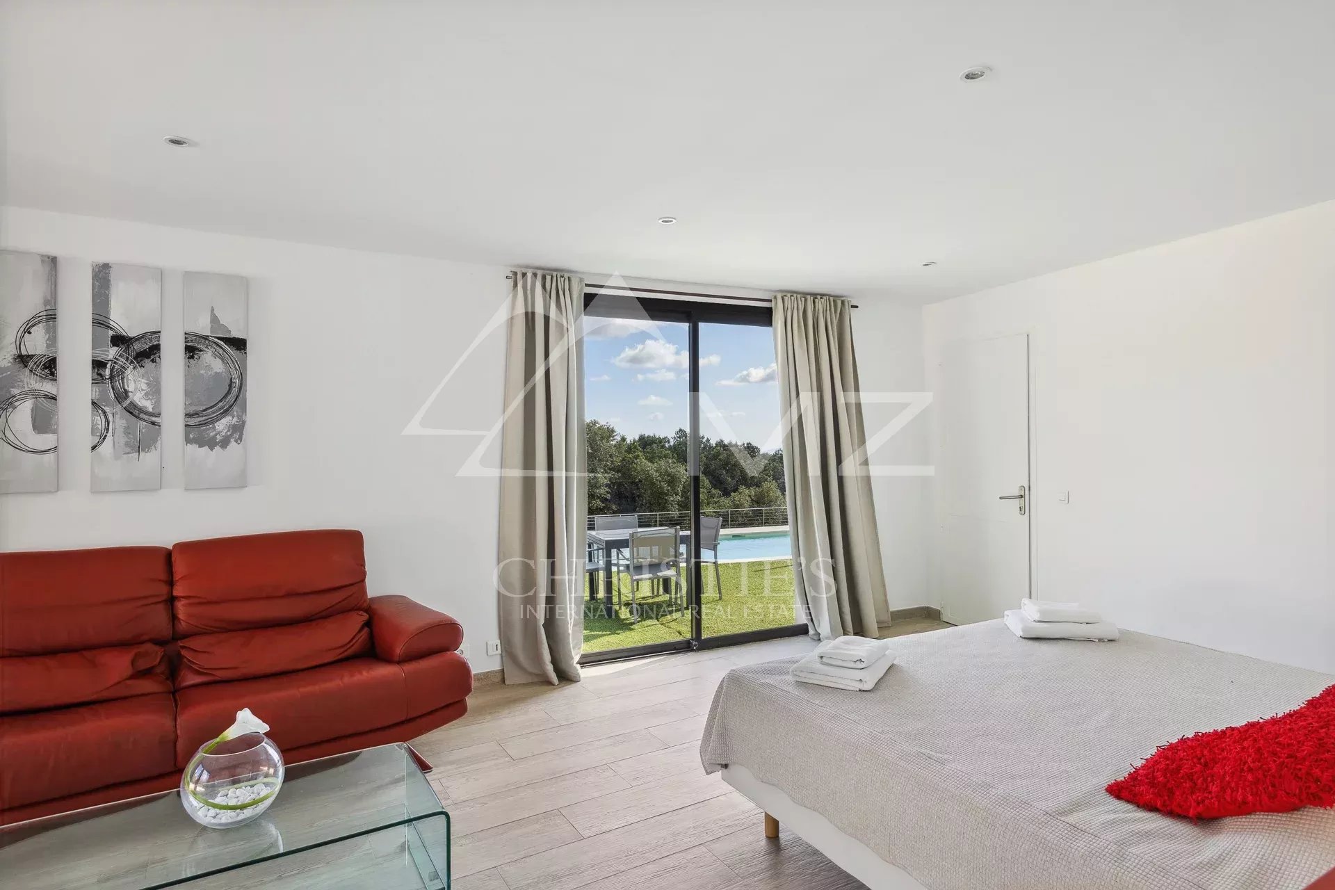 Bright room with pool view, red sofa and light bedding.