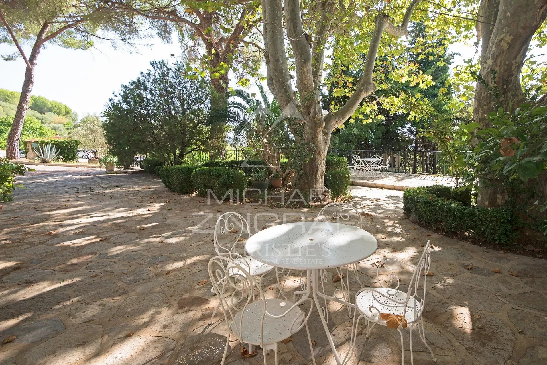 Terrasse de la bastide provençale Terrasse avec table et chaises en fer forgé sous des arbres, dans un domaine de figuiers à Solliès-Pont.