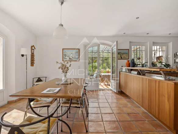Intérieur d'une bastide avec table en bois et baies vitrées donnant sur le jardin.