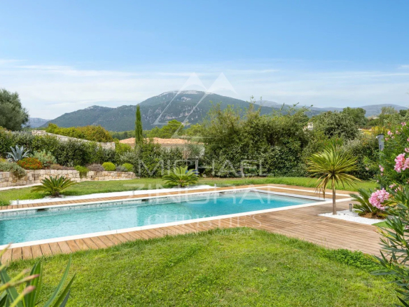 Vue de la piscine et du jardin d'une villa contemporaine à Roquefort-les-Pins avec des collines en arrière-plan.