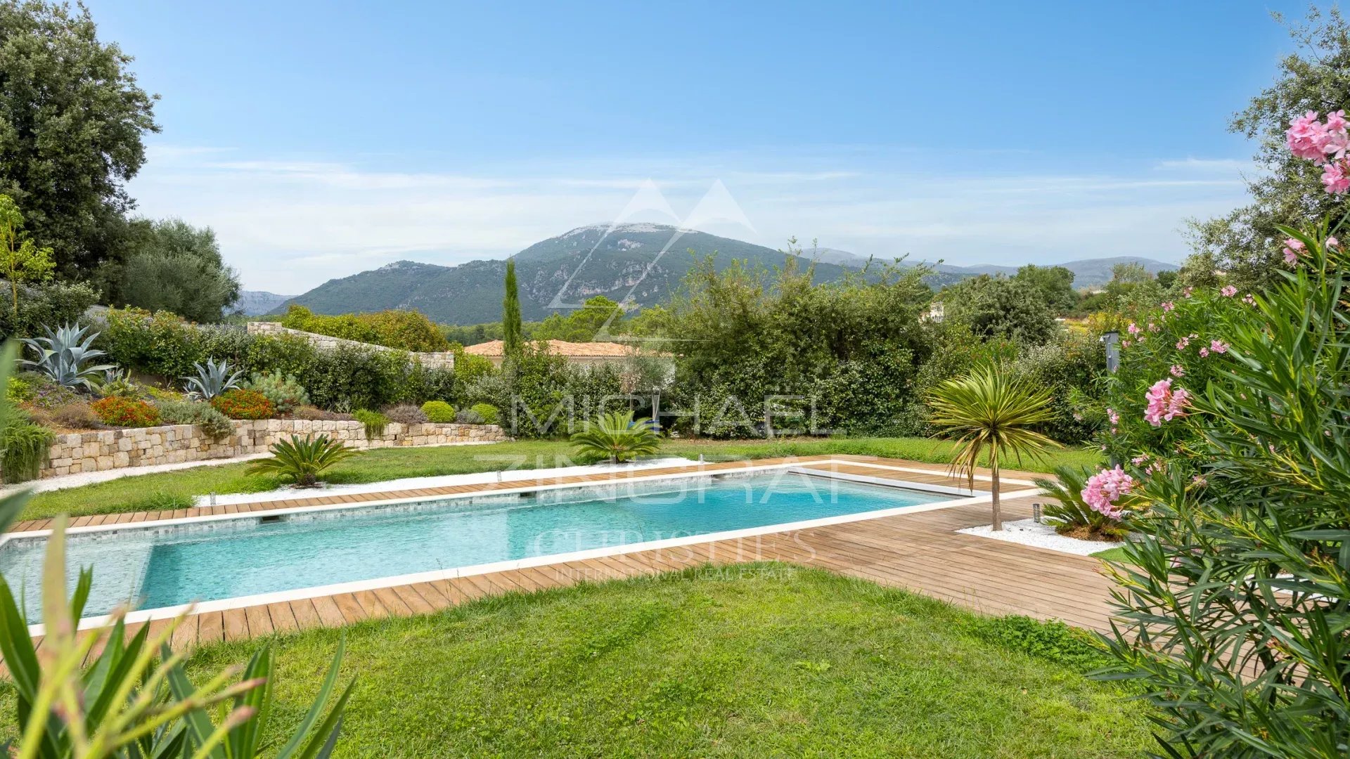 Villa contemporaine à Roquefort-les-Pins Vue de la piscine et du jardin d'une villa contemporaine à Roquefort-les-Pins avec des collines en arrière-plan.