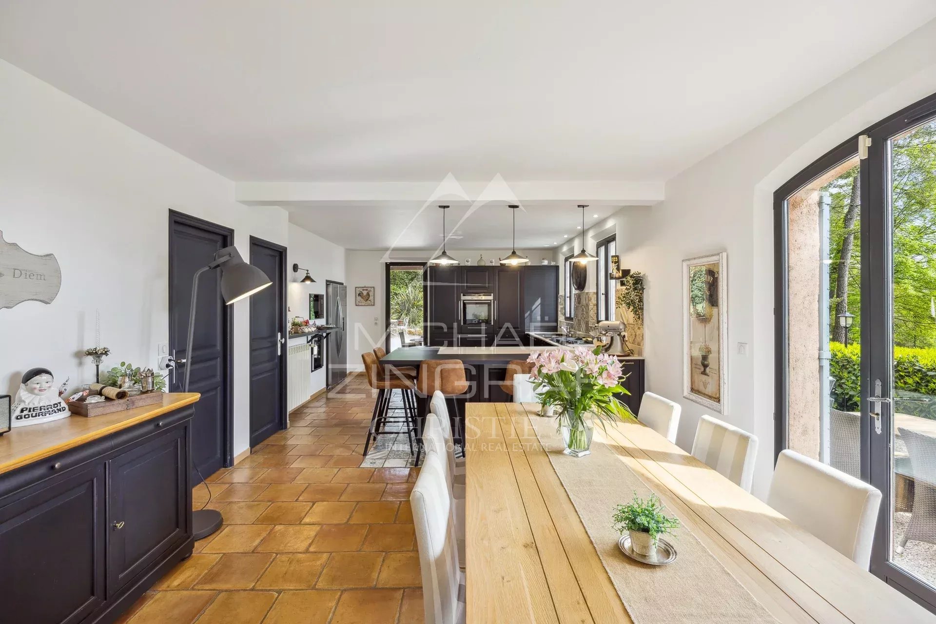 Interior of an elegant country house with a large wooden table and an open kitchen.