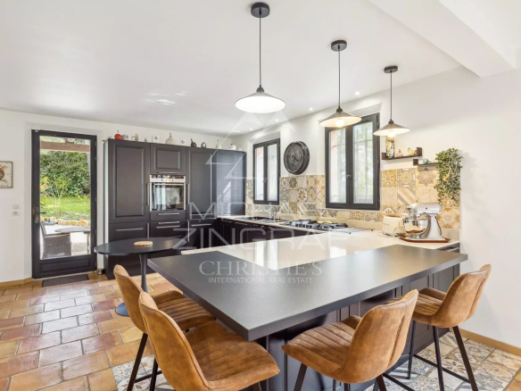 Modern and spacious kitchen with central island and leather chairs, open to the outside.