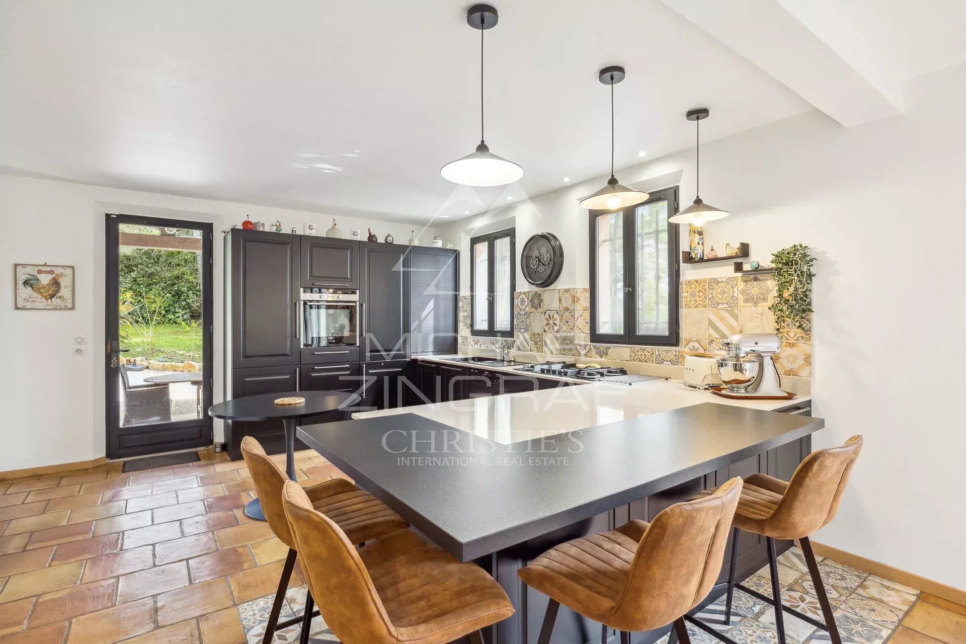 Modern and spacious kitchen with central island and leather chairs, open to the outside.