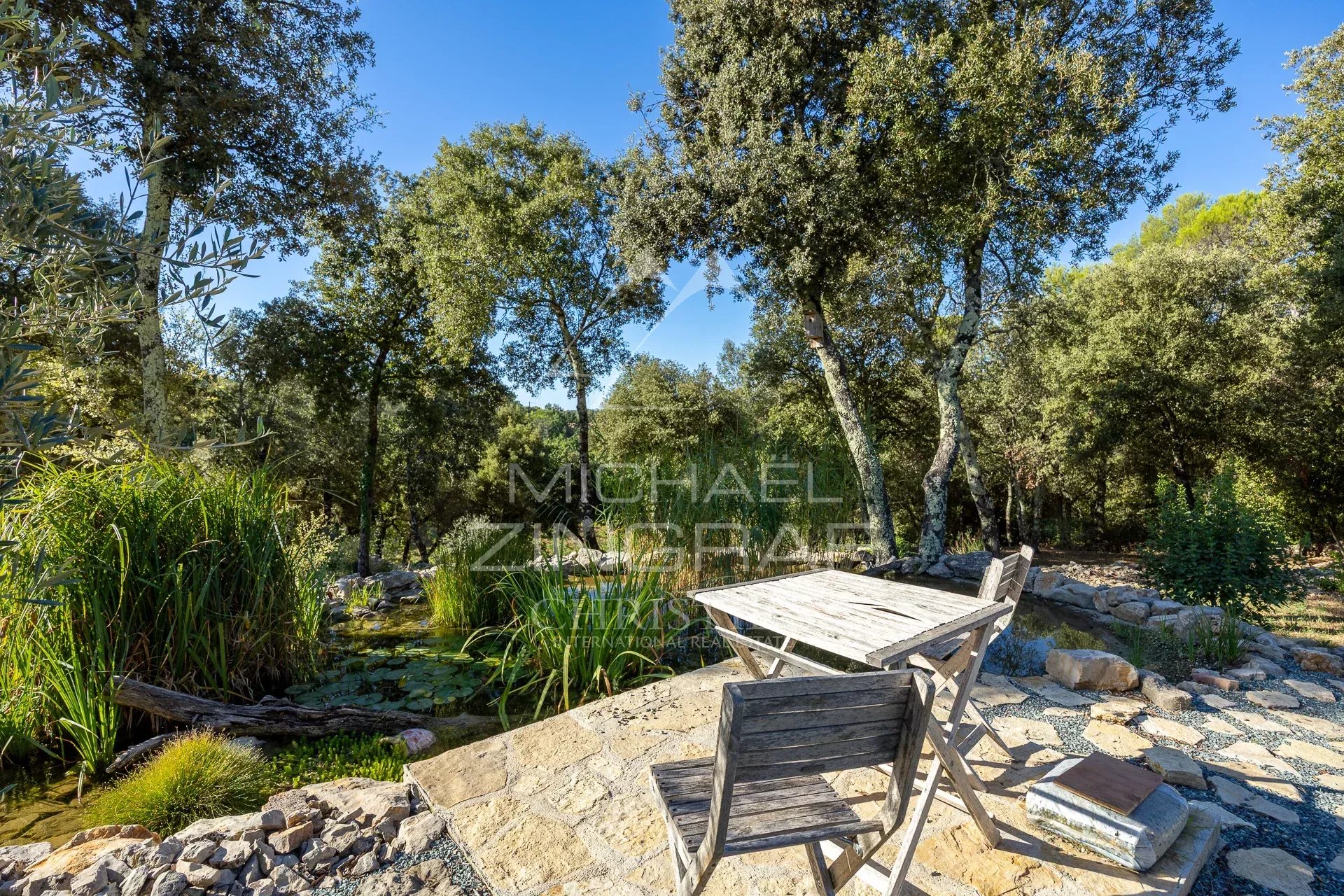 Espace extérieur en Provence Espace extérieur d'une propriété en Provence avec une table en bois entourée d'arbres et d'un plan d'eau.