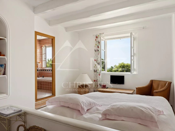 Chambre lumineuse avec fenêtre ouverte et vue sur la nature, fauteuil en cuir à côté du lit.