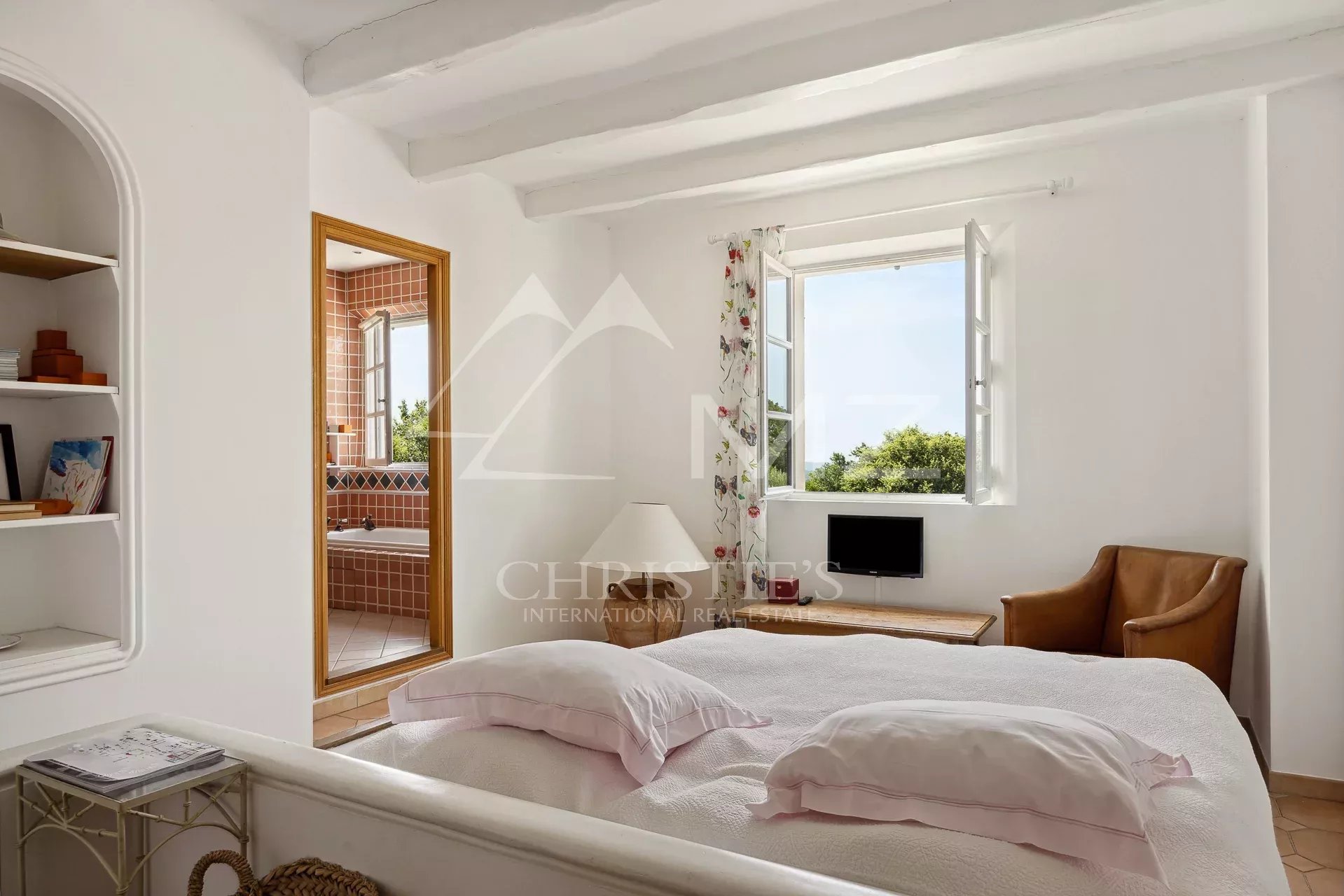 Chambre lumineuse dans une propriété provençale Chambre lumineuse avec fenêtre ouverte et vue sur la nature, fauteuil en cuir à côté du lit.