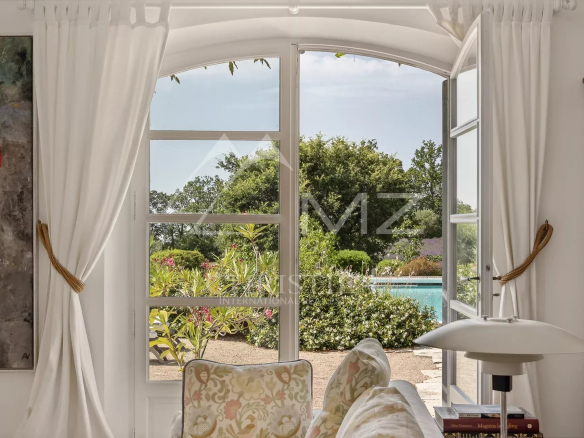 Vue intérieure d'une maison avec fenêtres ouvertes sur un jardin et une piscine.