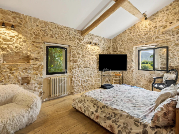 Chambre d'une demeure en pierre avec lit, fenêtres et décoration rustique.