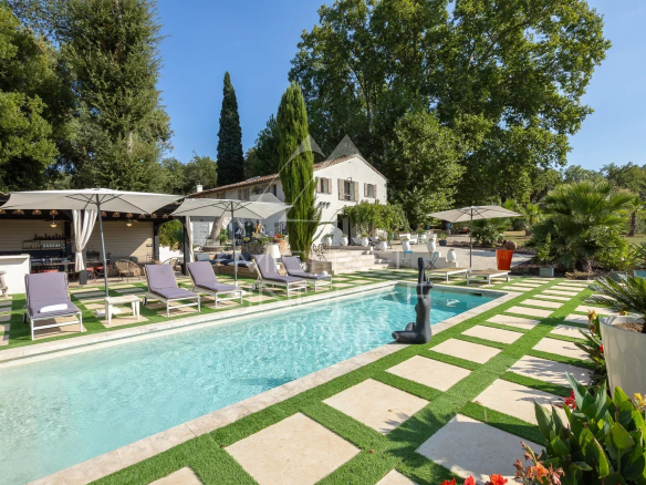 Demeure avec piscine et chaises longues, entourée de verdure et d'arbres.