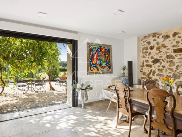 Intérieur d'une demeure avec table en bois et vue sur un jardin avec des chaises en fer forgé.