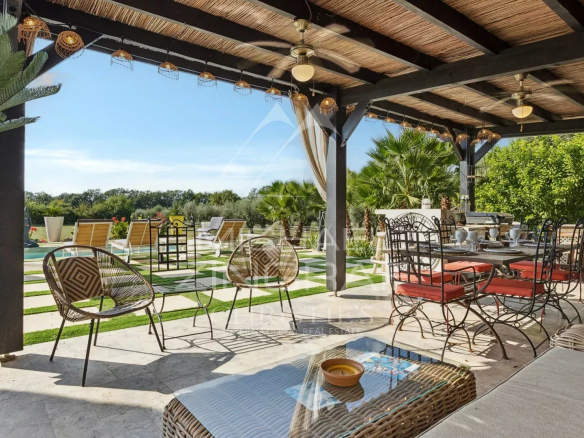 Terrasse d'une demeure avec piscine, chaises et tables, vue sur un jardin verdoyant