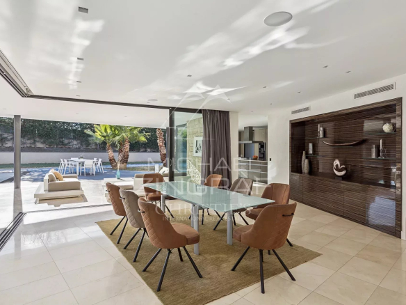 Salle à manger moderne avec grandes baies vitrées donnant sur une terrasse et une piscine.