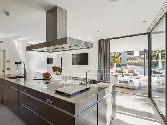 Cuisine moderne et spacieuse avec îlot central et baies vitrées donnant sur l'extérieur.