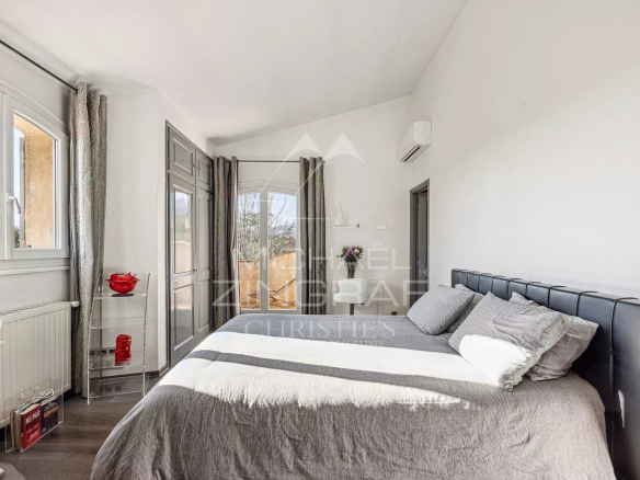 Chambre d'une villa provençale avec lit double et fenêtre laissant entrer la lumière naturelle.