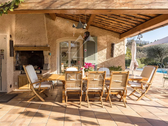 Terrasse en bois avec table et chaises, piscine et jardin en arrière-plan, dans une villa provençale.