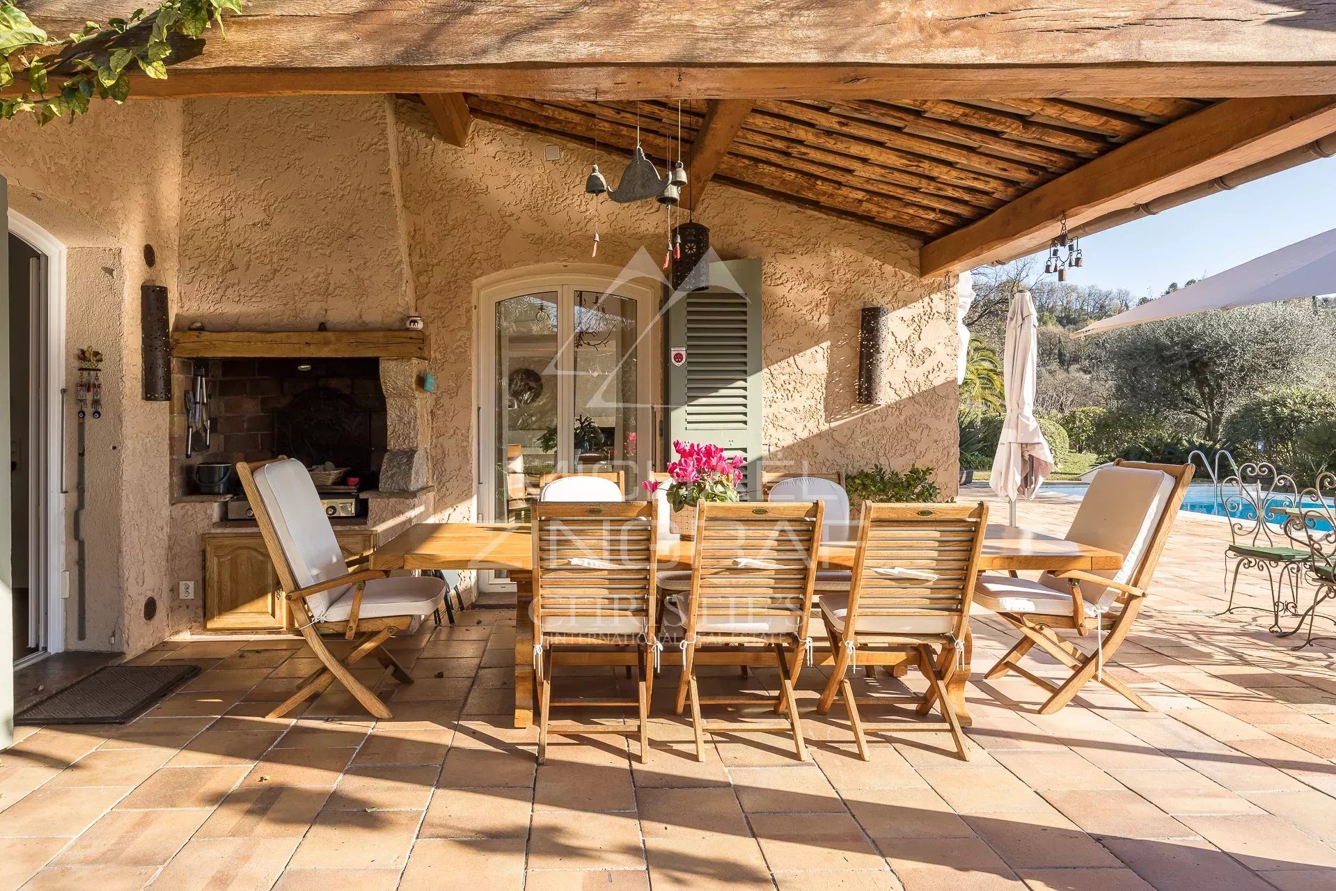 Terrasse d’une villa provençale Terrasse en bois avec table et chaises, piscine et jardin en arrière-plan, dans une villa provençale.