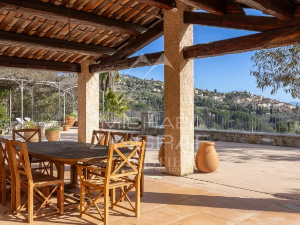 Terrasse ensoleillée avec table et chaises en bois, vue sur le village de Fayence.